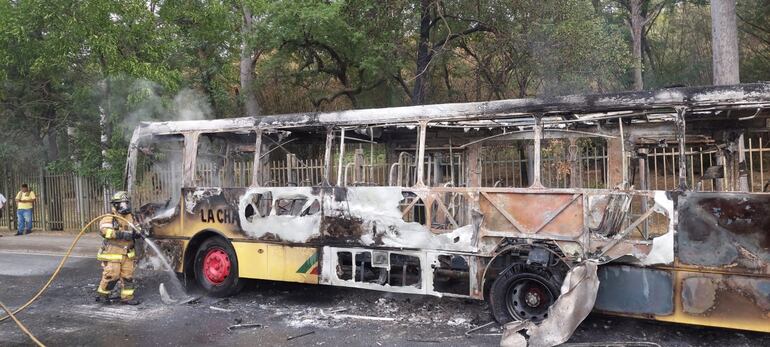 Un bombero termina de sofocar el fuego en el colectivo de La chaqueña reducido a una carcaza, frente al Jardín Botánico de Asunción.