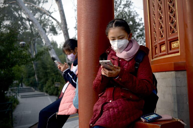 Dos niños con tapabocas miran su teléfono celular cerca de la ciudad prohibida de Pekín, en China. 