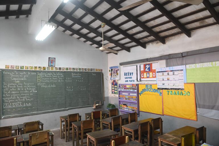 Salón de clases con muebles precarios y humedad en el techo en una escuela de Asunción.