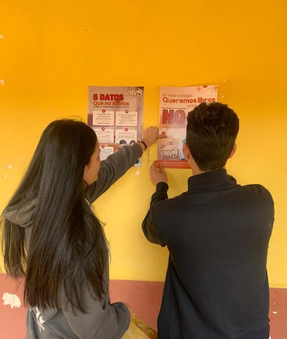 Estudiantes colocan flyers de la campaña "queremos libros para estudiar, no pañales para cambiar” en un colegio.