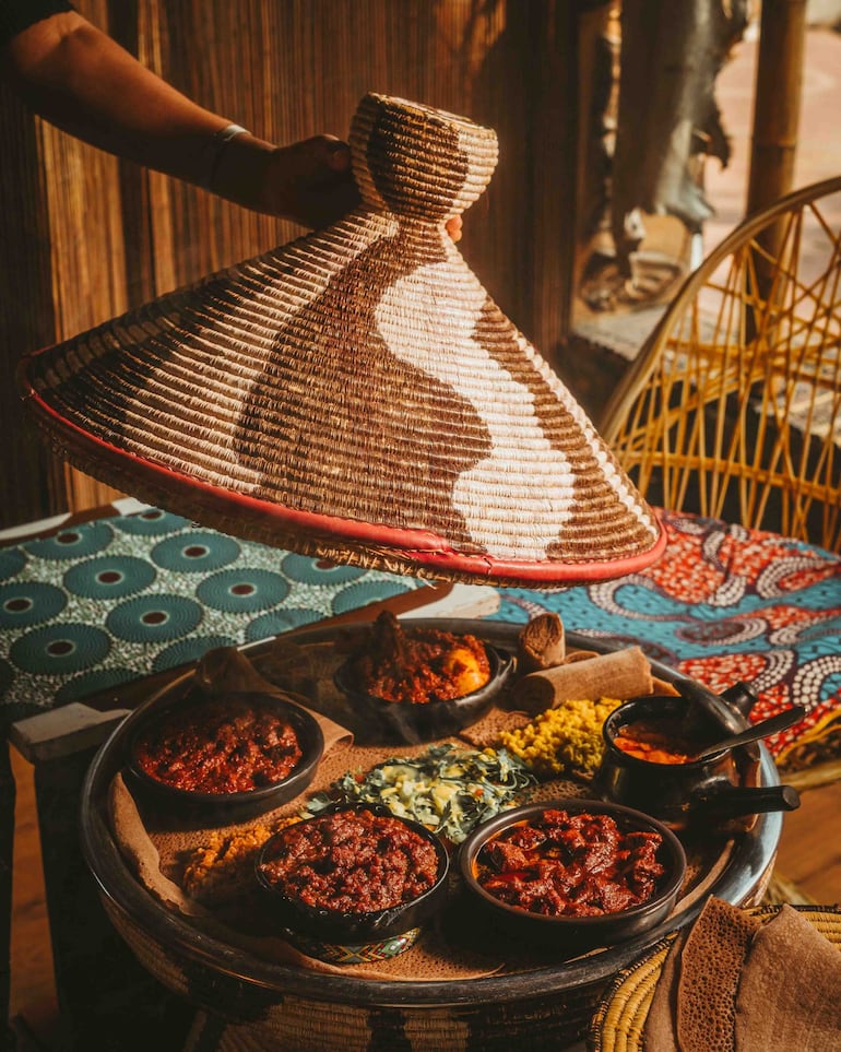 Varias carnes en cuencos de cerámica condimentadas con salsa roja acompañadas de salsa amarilla de lentejas sobre "Injera", un pan plano tipo pita típico del este de África.