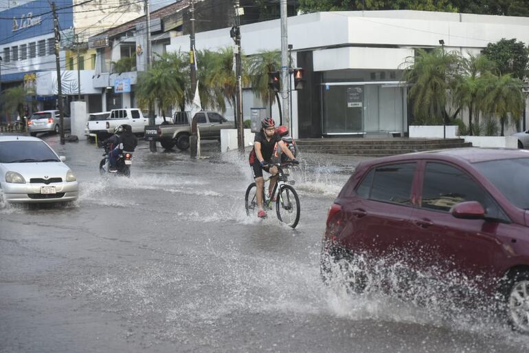 Un ciclista circula por Asunción en su bicicleta, sorteando vehículos a motor en un raudal.