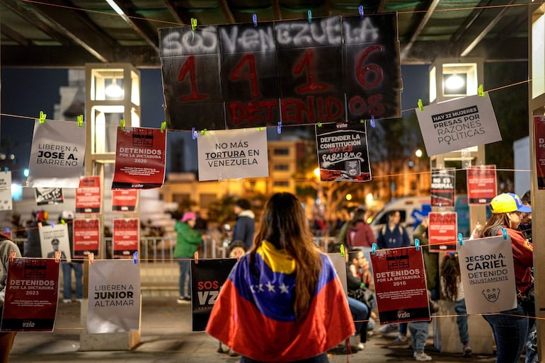 Una persona con bandera de Venezuela observa unos carteles durante una protesta