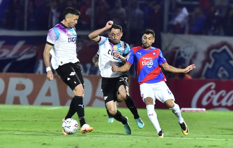 Federico Carrizo disputa la tenencia de la pelota con Iván Piris, Álvaro Campuzano completa la imagen.