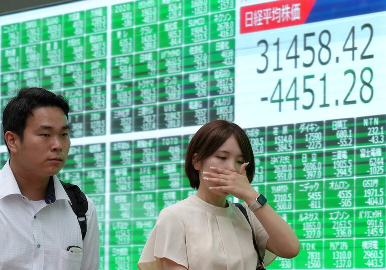 Peatones pasan junto a un cartel que exhibe información sobre el nikkei en la bolsa de valores, con su mayor pérdida de la historia en Tokio, Japón.