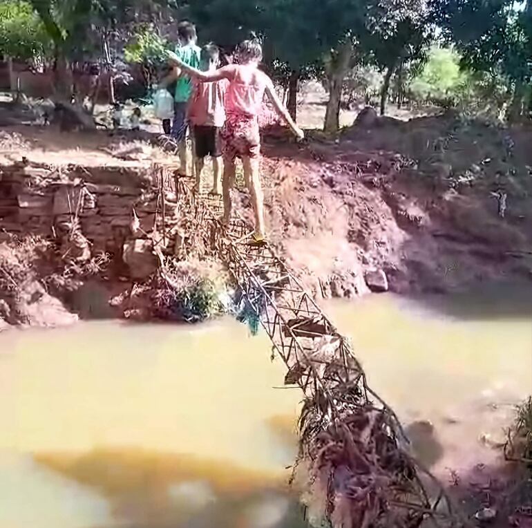 Los niños se arriesgan para cruzar la viga de metal que quedó tras el colapso del puente.