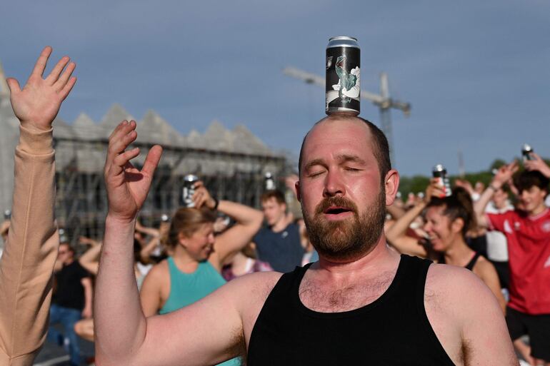 Un hombre hace equilibrio con una lata de cerveza en la cabeza, mientras se las arregla para mantener la postura del árbol. 