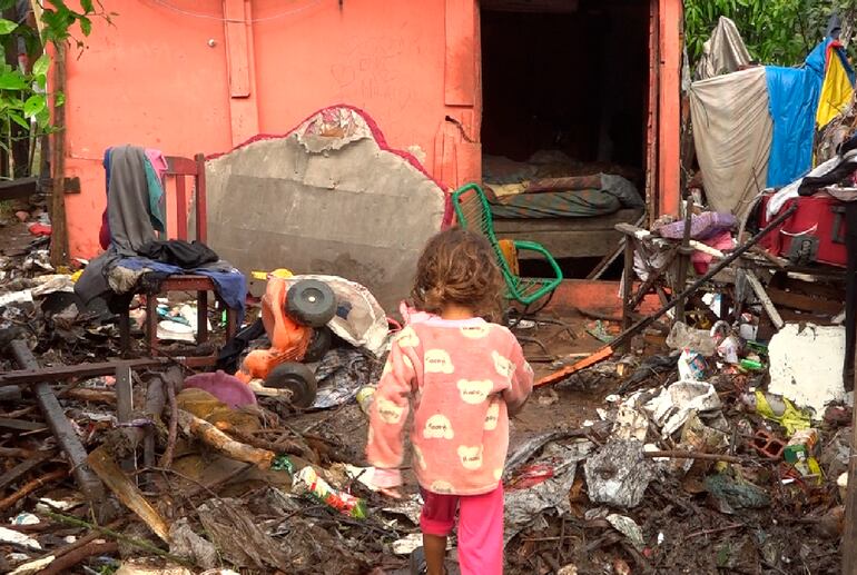 Niña entra a su precaria casa que se muestra abarrotada de basura traida por al raudal. La misma se ve obligada a vivir en un lugar insalubre.