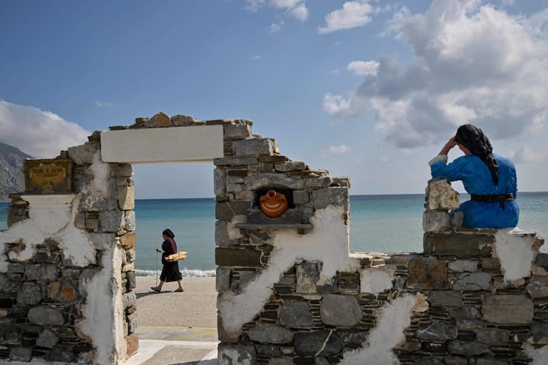 Una mujer que transporta madera recolectada camina frente a una escultura dedicada a las mujeres en Diafani, la aldea portuaria de Olympos, en la isla de Cárpatos. 