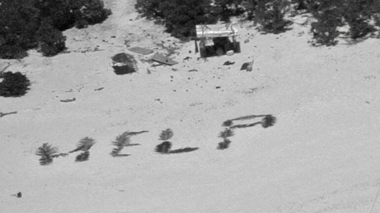 Esta imagen obtenida de la Guardia Costera de EE. UU. el 11 de abril de 2024 muestra un cartel de "Ayuda" en la playa hecho con hojas de palma por tres marineros varados en el atolón Pikelot, estado de Yap, Estados Federados de Micronesia.