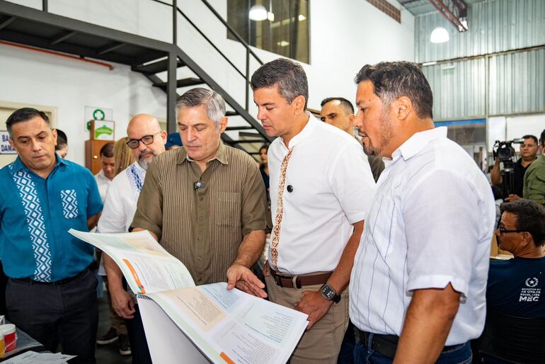 El ministro de Educación, Luis Ramírez, muestra libros de texto al presidente Santiago Peña.