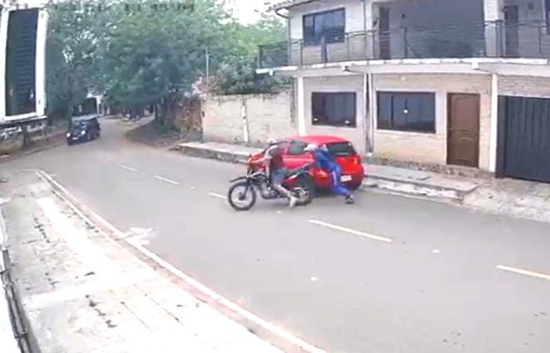 Momento que dos personas se alzan con la motocicleta y en el fondo se ve el vehículo en el que habían llegado.