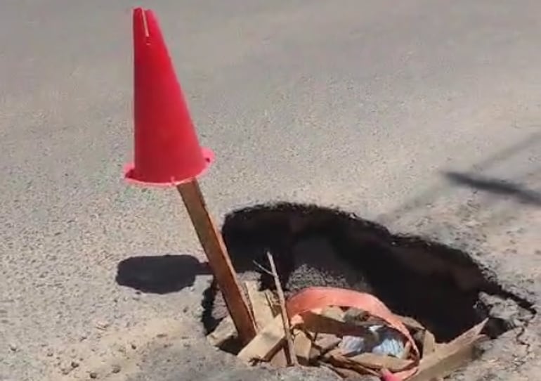 Un palo con un cono para señalizar el bache que en su interior hay madera y otros elementos.