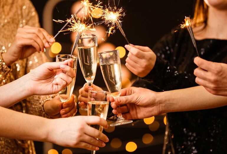 Manos de mujeres brindando con copas de champán y estrellitas.