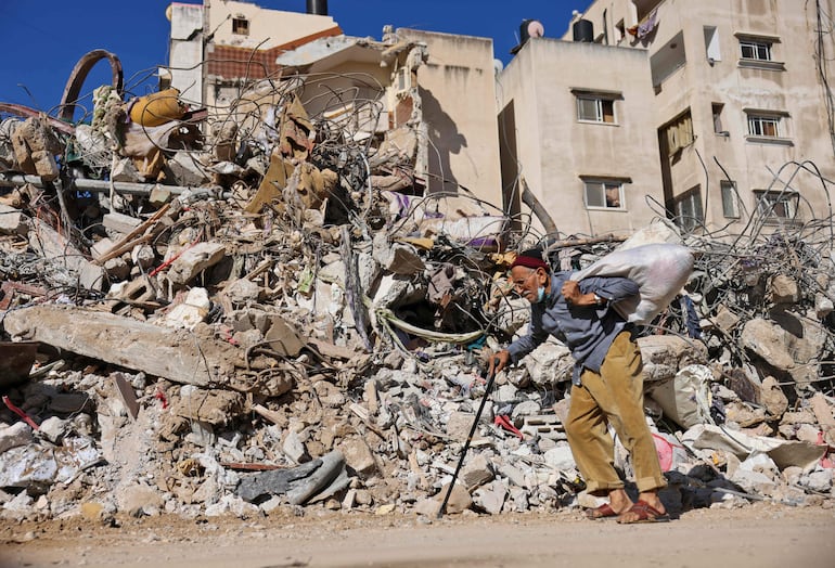 TOPSHOT - A Palestinian elderly man walks past a building destroyed by Israeli bombardment in Gaza City, on May 19, 2021 - Deafening air strikes and rocket fire once more shook Gaza overnight and early today amid an international diplomatic push to broker a ceasefire after more than a week of bloodshed. Warplanes hit Gaza City again in the pre-dawn hours, with the Israeli military continuing to target Palestinian militant leaders and infrastructure in the crowded enclave, under Israeli blockade for nearly 15 years. (Photo by MOHAMMED ABED / AFP)