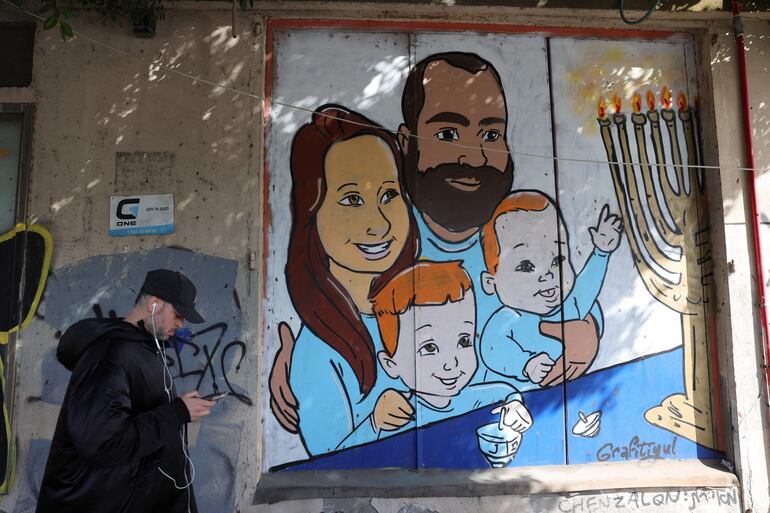 Un hombre pasa junto a un graffiti de la familia Bibas en Tel Aviv, Israel. El 20 de febrero, Hamás entregó los cuerpos de cuatro cautivos israelíes, incluido el del rehén más joven, Kfir Bibas, como parte del actual acuerdo de alto el fuego en Gaza. Hamás dijo en noviembre de 2023 que los dos niños Bibas y su madre habían muerto en un ataque aéreo israelí en Gaza. 