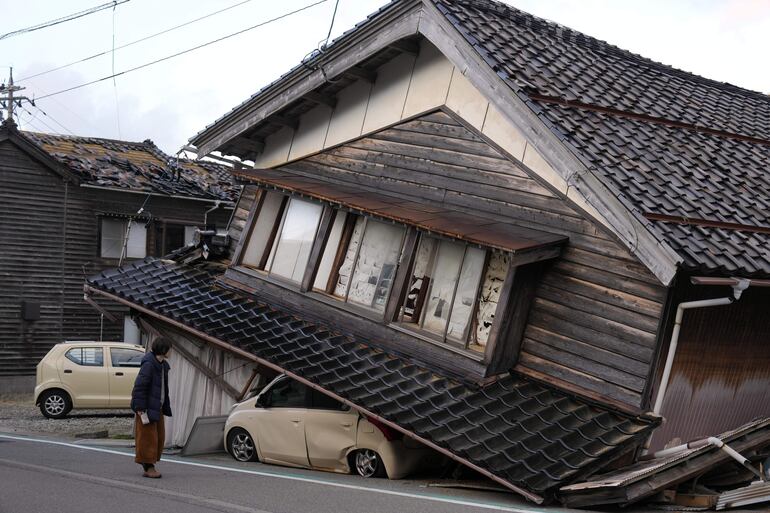 Una mujer observa una vivienda y vehículos dañados tras un fuerte terremoto en Tohi Town, en la península de Noto, Japón.