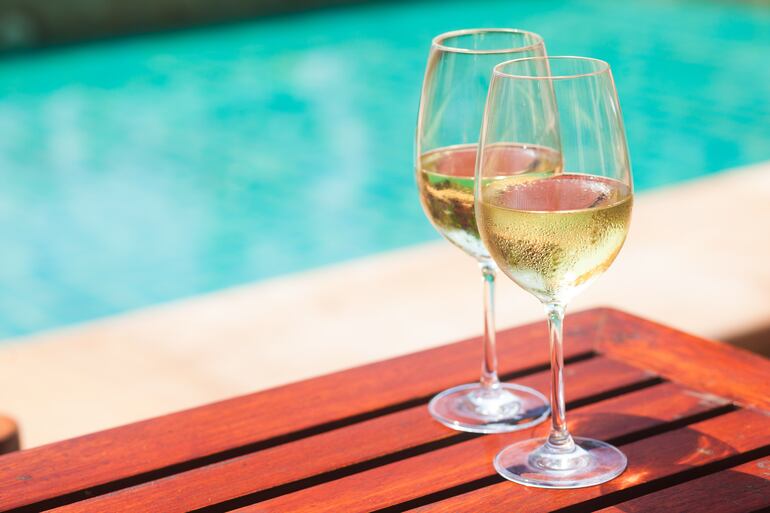 Dos copas de vino blanco frío sobre un deck de madera junto a una piscina.