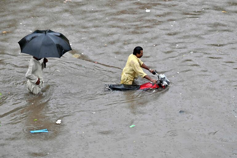 Un motociclista empuja su bicicleta por una calle inundada después de fuertes lluvias en Lahore.
