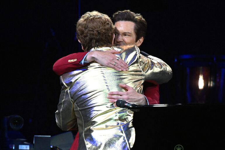 Elton John se abraza con el cantante Brandon Flowers en el escenario. 