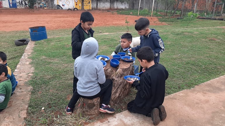 Un tronco de madera es utilizada por los niños para almorzar. En la imagen se ve a una niño arrodillado debido a la falta de una silla.