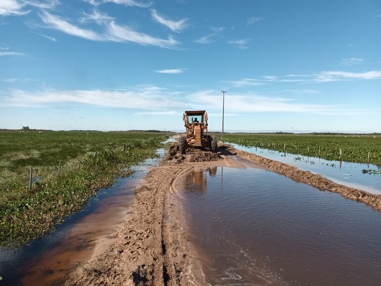 Una vieja y solitaria motoniveladora del MOPC intenta reparar el camino que se encuentra llena de agua en la zona de Duarte Cué entre el distrito de Tacuaras y Guazucuá.