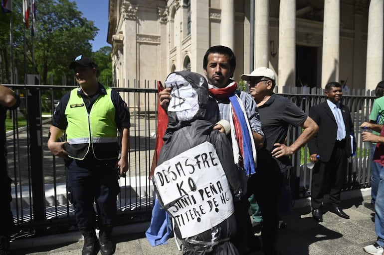 Con un muñeco que lleva un cartel con la leyenda "Desastre ko Santi Peña, títere de HC", un nombre se manifiesta frente al Panteón Nacional de los Héroes contra la ley que crea la Superintendencia de Jubilaciones y Pensiones.