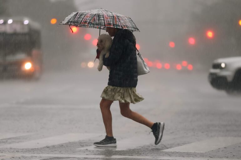 Una mujer carga a su perro mientras corre en medio de la lluvia este miércoles, en Buenos Aires (Argentina). La capital argentina, Buenos Aires, y la provincia homónima amanecieron este miércoles con alerta por fuertes tormentas y vientos, que han causado daños materiales y la cancelación de vuelos en los principales aeropuertos. EFE.