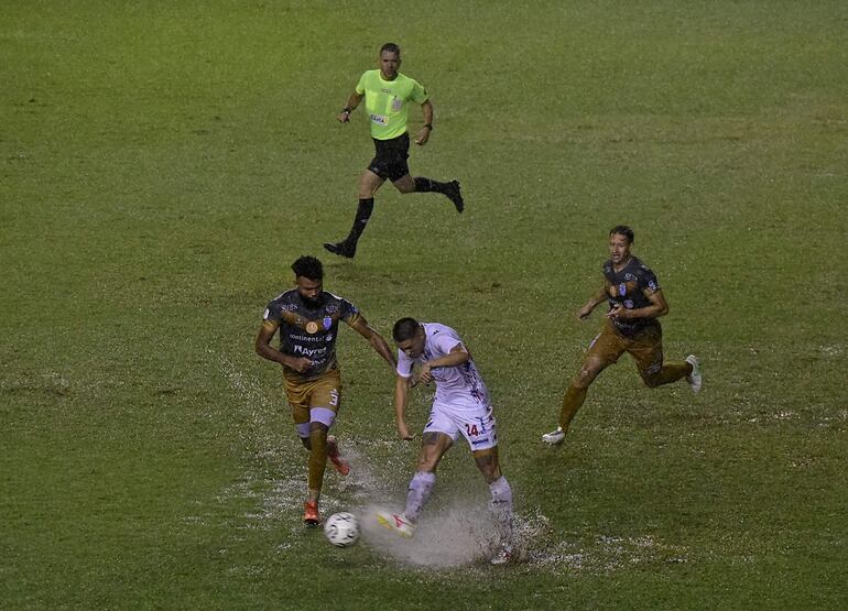 Jordan Santacruz salpica agua y barro al despjar el balón con un puntín ante la presión del defensor de Ameliano Thomás Gutiérrez.