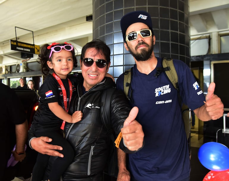 Óscar Santos Peralta con su hija en brazos, posa junto a Jorge Frutos, otro paraguayo que fue también protagonista en el Dakar 2024, y que se sumó al grupo de mecánicos del prestigioso equipo South Racing.