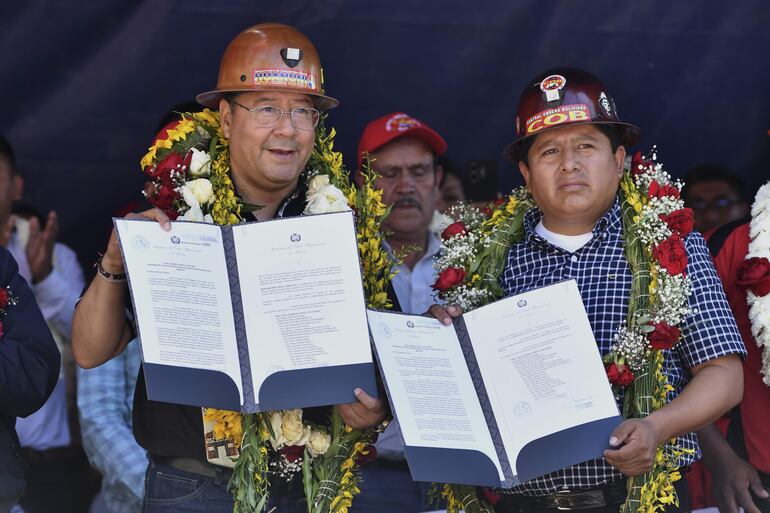 El presidente de Boliviano, Luis Arce (i), muestra el proyecto que envió al Legislativo para elevar a rango de ley un decreto de 2022 que regula la aplicación de los derechos laborales adquiridos por los trabajadores, durante un acto en conmemoración del Día Internacional de los Trabajadores.