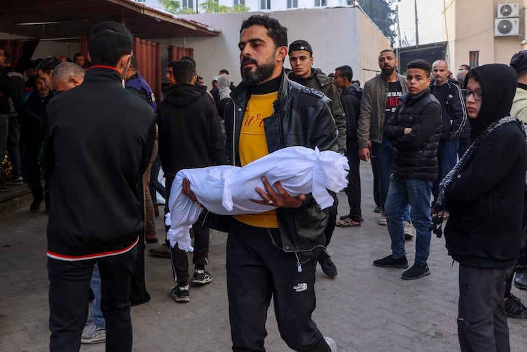 Un hombre lleva el cuerpo sin vida de un bebé muerto en un bombardeo israelí anoche en Ciudad de Gaza.