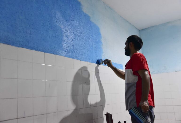 Un padre de familia pinta el sanitario de la escuela República del Brasil.