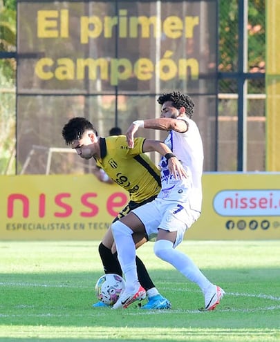 El aurinegro Richard Prieto intenta zafar de la férrea marca de Alejandro Samudio de Ameliano, en el empate de ayer en Dos Bocas.