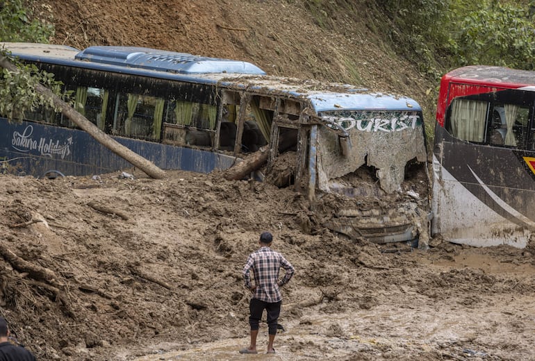 Un hombre observa buses parcialmente enterrados por un deslizamiento de tierra a consecuencia de las fuertes lluvias, este domingo en la localidad de Dadhing, Nepal.