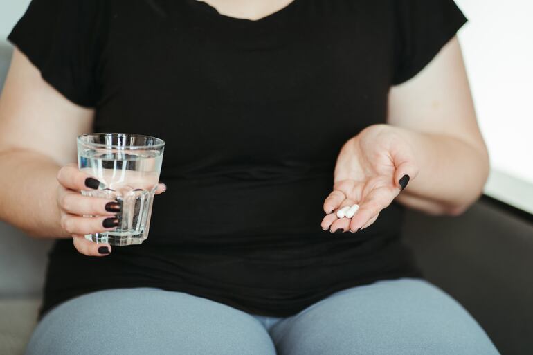 Torso de una mujer obesa sentada con un vaso de agua en una mano y dos píldoras en la ortra.