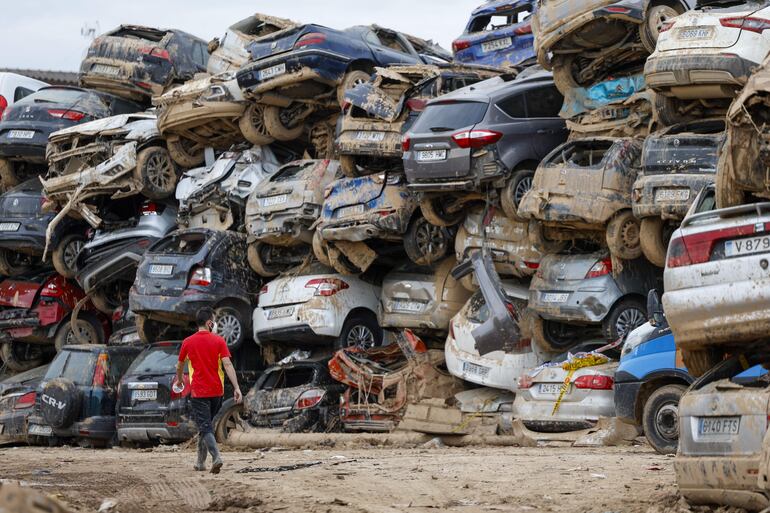 Un voluntario camina junto a una pila de vehículos destrozados en Paiporta, este martes. La DANA que dejó en Valencia más de dos centenares de muertos ha cambiado la vida de miles de personas.