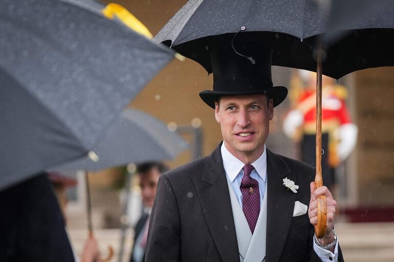 El Príncipe Guillermo de Gran Bretaña llegando con un paraguas a la Fiesta en el Jardín del Soberano, en el Palacio de Buckingham.