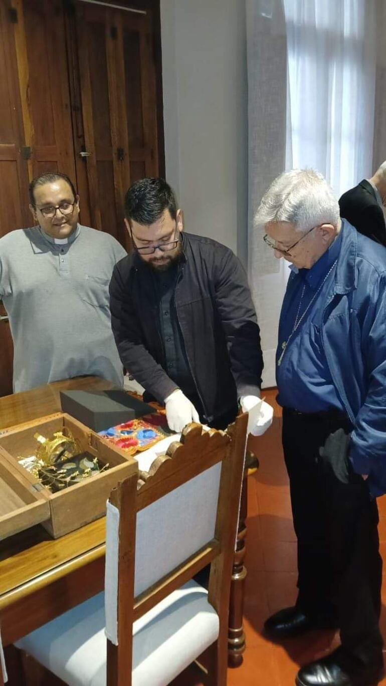 Sobre la mesa se puede apreciar una caja de madera, dentro las joyas de oro. Se aprecia la corona y otros accesorios.