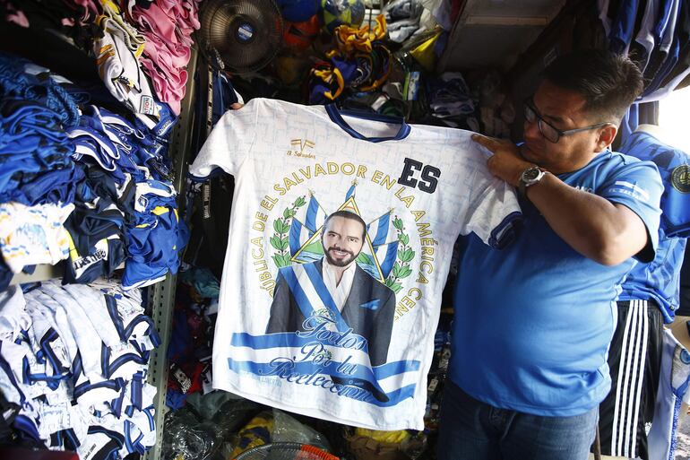 Un hombre muestra una camiseta con la imagen del presidente de El Salvador, Nayib Bukele, en un puesto de venta, en San Salvador (El Salvador). 