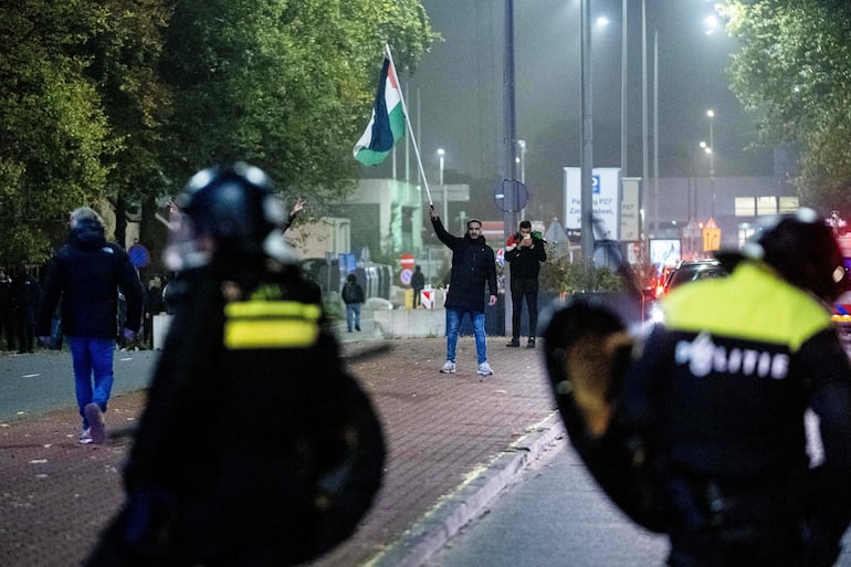 Un partidario ondea una bandera palestina frente a agentes de policía de la Unidad Móvil (ME) durante una manifestación pro palestina al margen del partido de fútbol de la Liga Europea de la UEFA entre el Ajax Amsterdam y el Maccabi Tel Aviv, en Amsterdam.