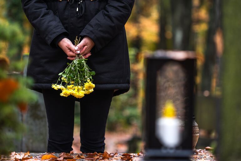 viuda frente a una tumba en el cementerio, con un ramo de flores amarillas en las manos