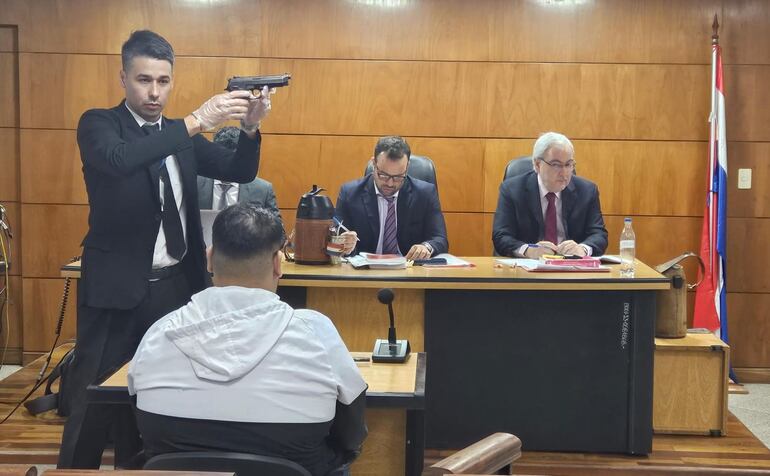 Un funcionario judicial exhibe el arma que según el testigo fue utilizada para asesinar a Robert. Al fondo, los magistrados Federico Ortiz y Héctor Fabián Escobar.