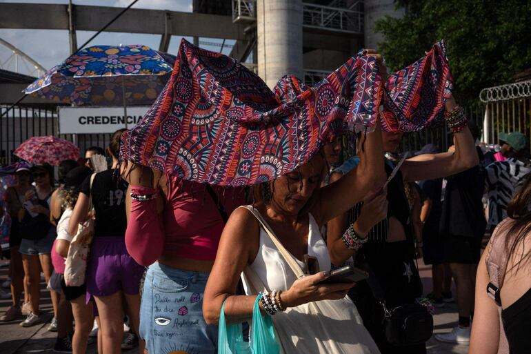 Personas intentaron cubrirse del intenso calor en Río de Janeiro cuando querían participar del concierto de Taylor Swift. (Photo by Tercio TEIXEIRA / AFP)