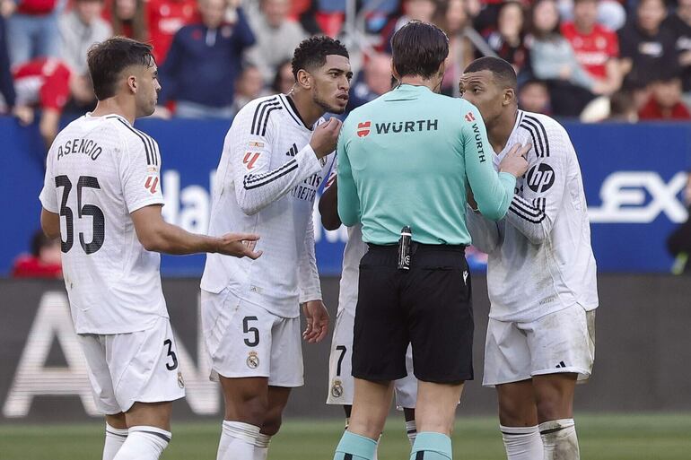 El delantero francés del Real Madrid Kylian Mbappé y su compañero el delantero inglés Jude Bellingham conversan con el árbitro Munuera Montero, en el juego ante el Osasuna, donde fue expulsado el inglés.
