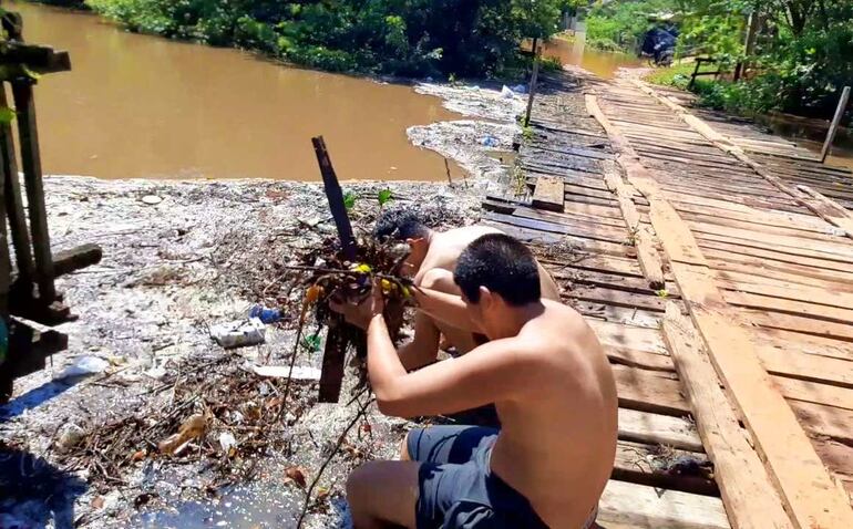 Dos adolescentes tratando de limpiar las basuras que quedaron estancadas en el precario puente de madera que tiene la comunidad y atrae miles de insectos.