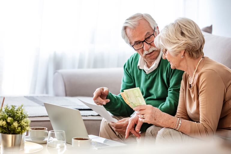 Un hombre y una mujer de la tercera edad hacen cálculos en una computadora.