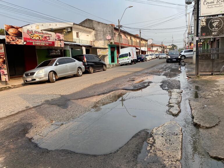 Gran bache lleno de agua en frente de diferentes negocios de la zona comercial.