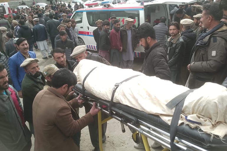 Varias personas trasladan el cuerpo de uno de los pasajeros fallecidos del bus que cayó a un río este miércoles en Pakistán.