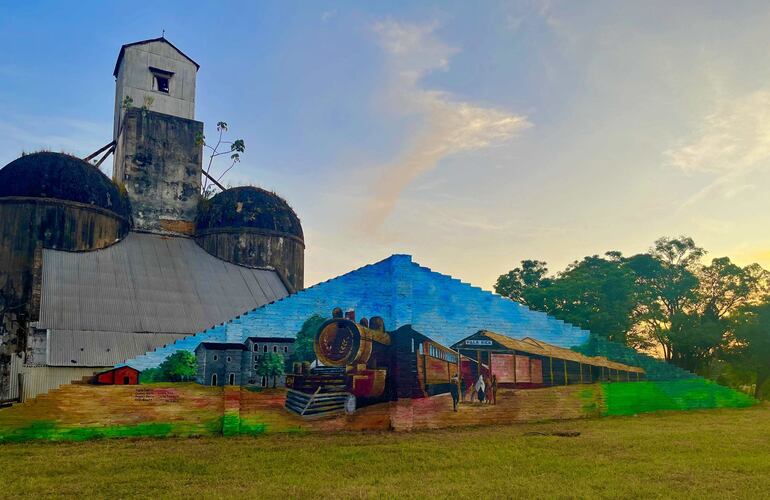 Mural con pintura del ferrocarril en la exestación de trenes de la ciudad de Villarrica, con el antiguo silo de fondo. 